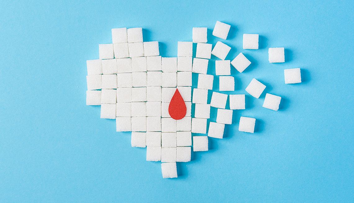 A drop of blood on a broken heart made of pure white cubes of sugar isolated on blue background.