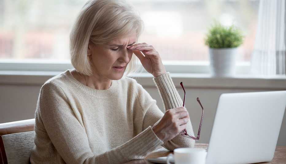 Mature woman rubs her irritated eyes after prolonged use of her computer