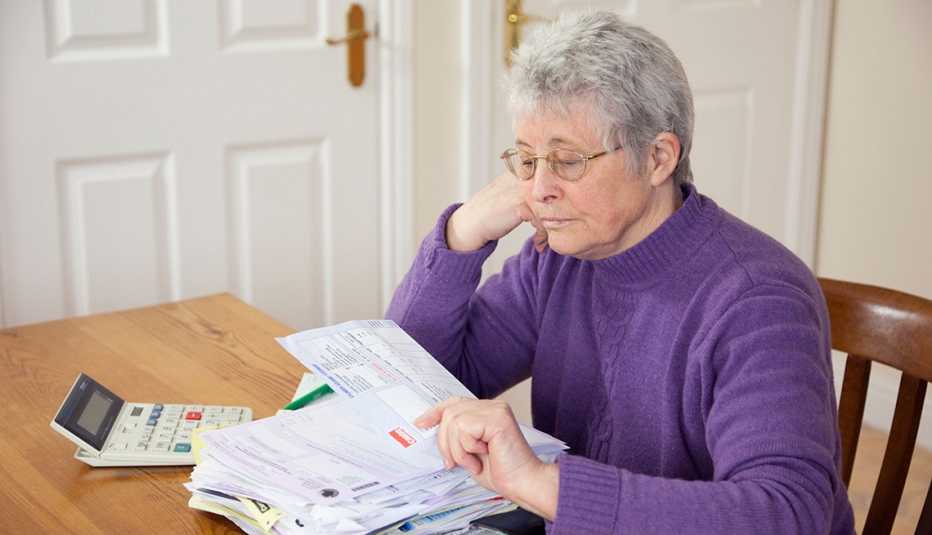 A woman sitting down and looking her stack of bills on a table