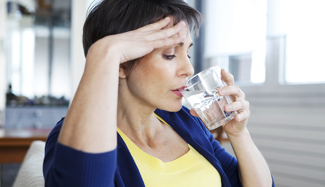 A woman experiencing hot flashes drinks water to cool down