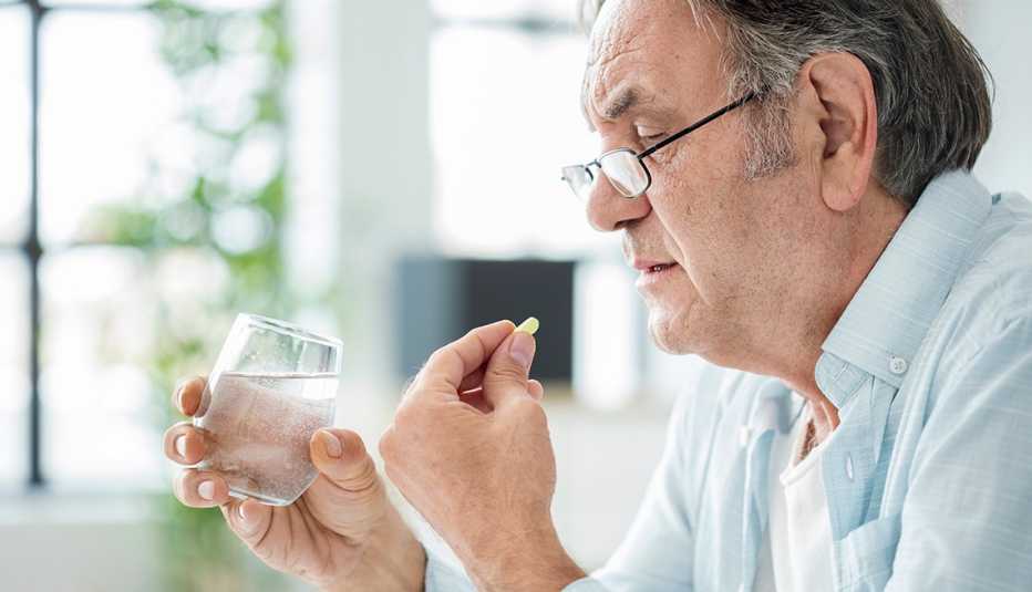 Older man taking a pill with a glass of water.