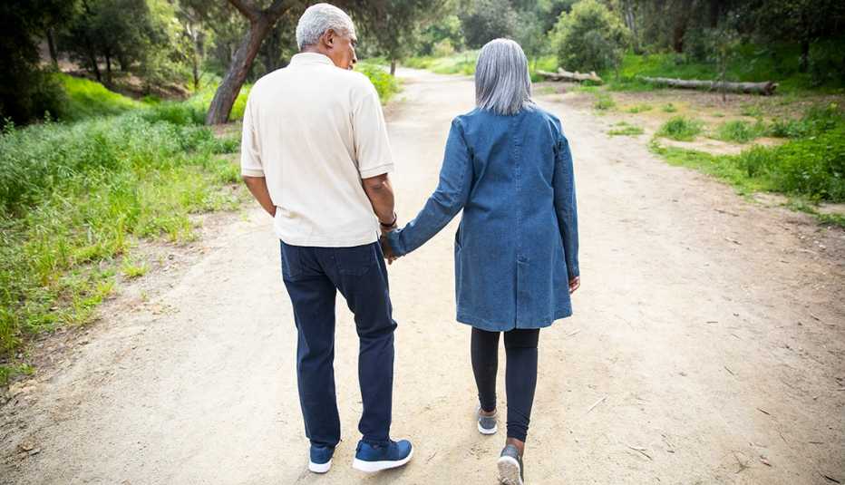 An older couple is walking down a path holding hands