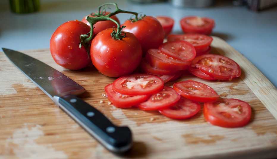 Whole and sliced tomatoes on a cutting board with a knife.