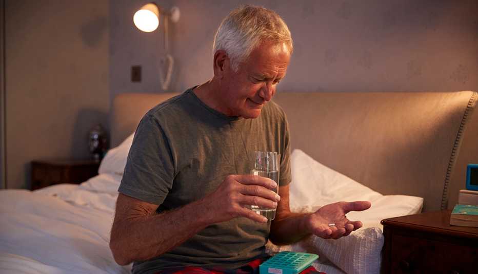 A man sitting on his bed at home holding a glass of water ready to take his medication