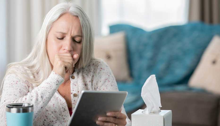 Older woman coughing while holding a tablet