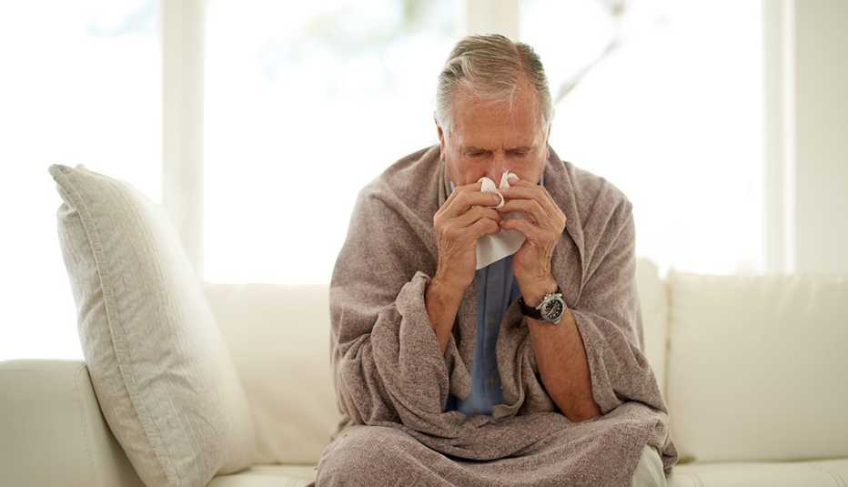 Shot of a senior man blowing his nose with a tissue at home