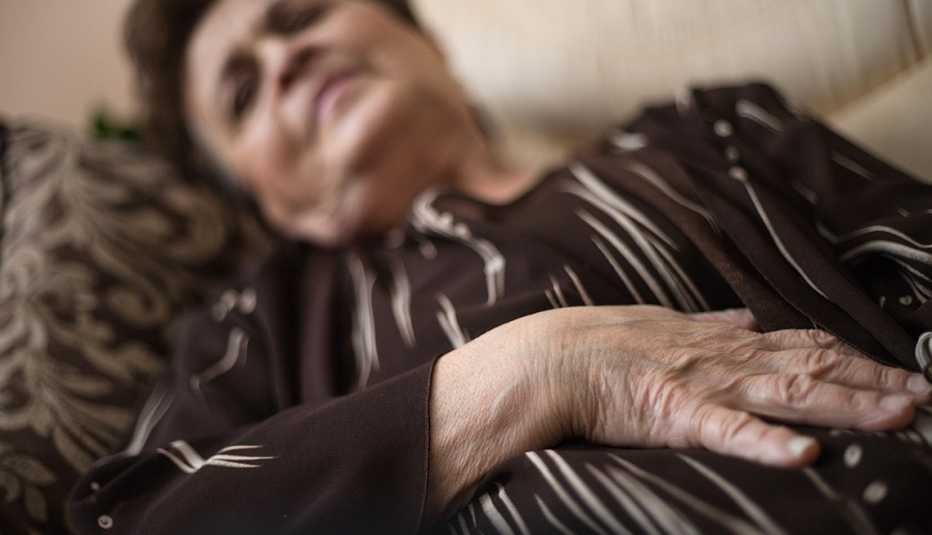 Mature woman is lying on the sofa in pain with stomach problems