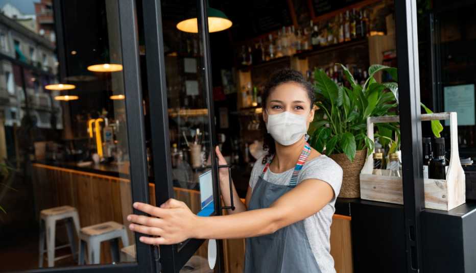 business owner opening the door of her restaurant while wearing face mask