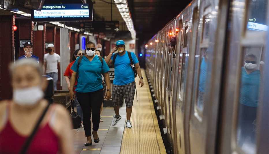 People wearing protective masks walk through the Essex Street subway station in New York