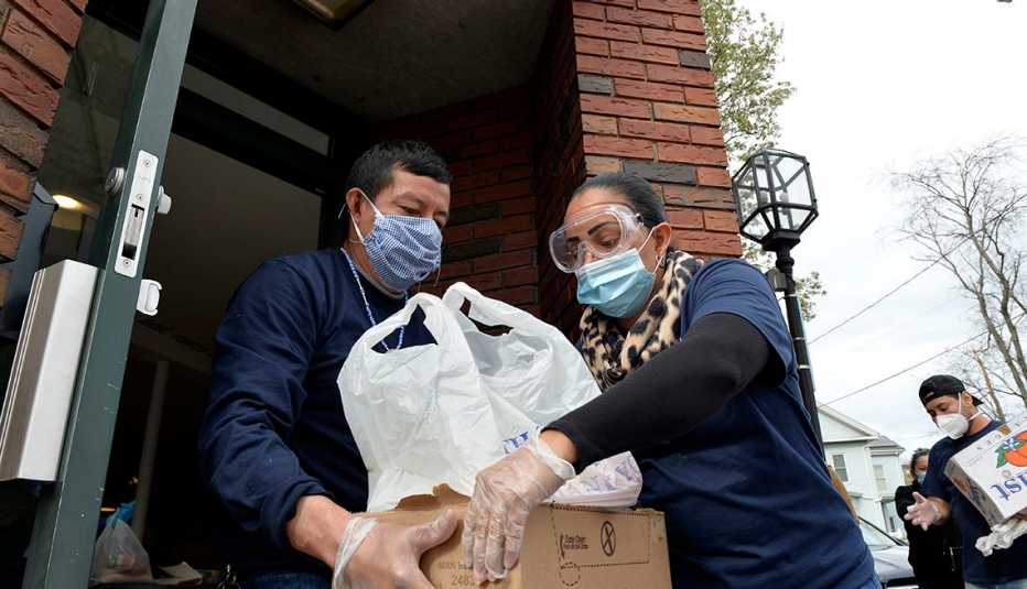 A man handing donated food to a woman to help people in the Hispanic community with coronavirus. Both are wearing face masks.