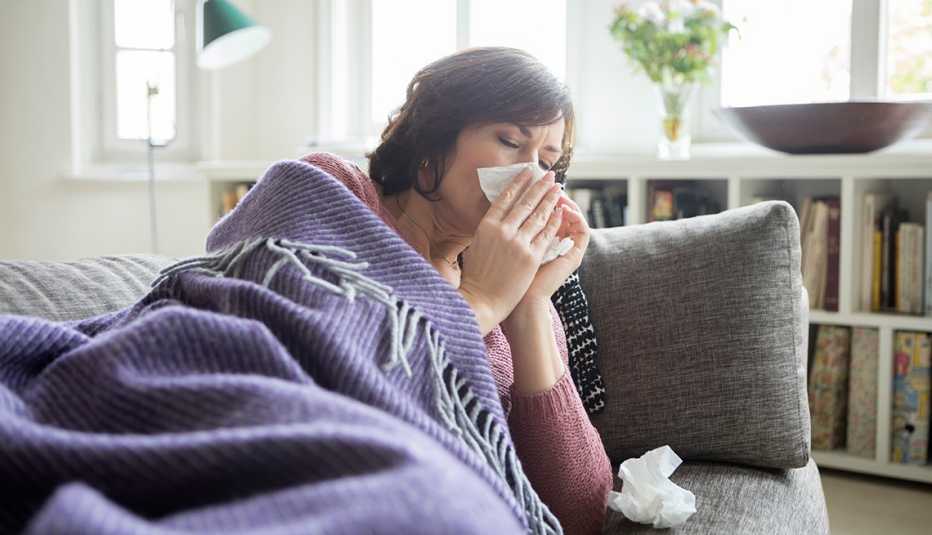Woman blowing nose under blanket, laying on couch