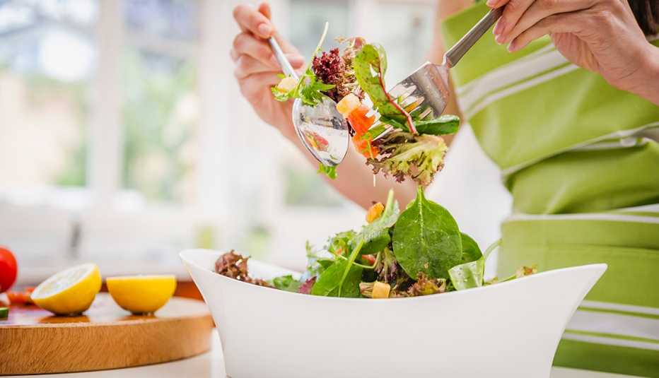  a woman tosses a fresh healthy looking salad with lemon dressing at home in her kitchen