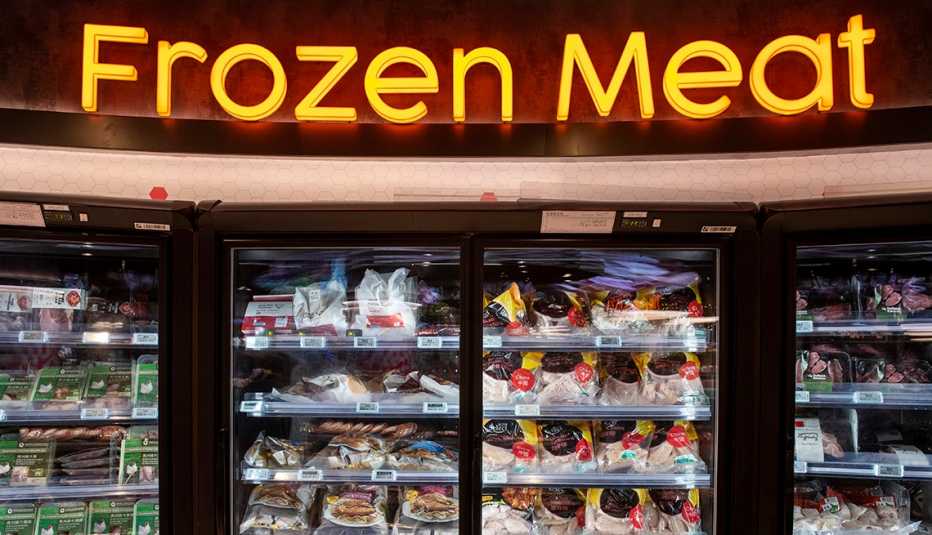 Display case of frozen meats with a sign saying frozen meat above the freezers.