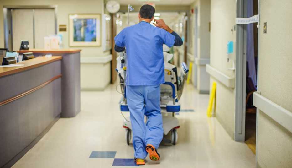 hospital employee with his back to us rolls a stretcher down a corridor