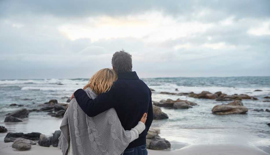 A couple hugging on winter beach looking at the ocean and clouds