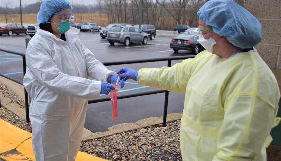 Franciscan Health Crown Point  Nurse Tambi Kieta (left in white) accepts a COVID-19 test sample from fellow nurse Jennifer Homan (right, in yellow), manager of Trauma Services there.