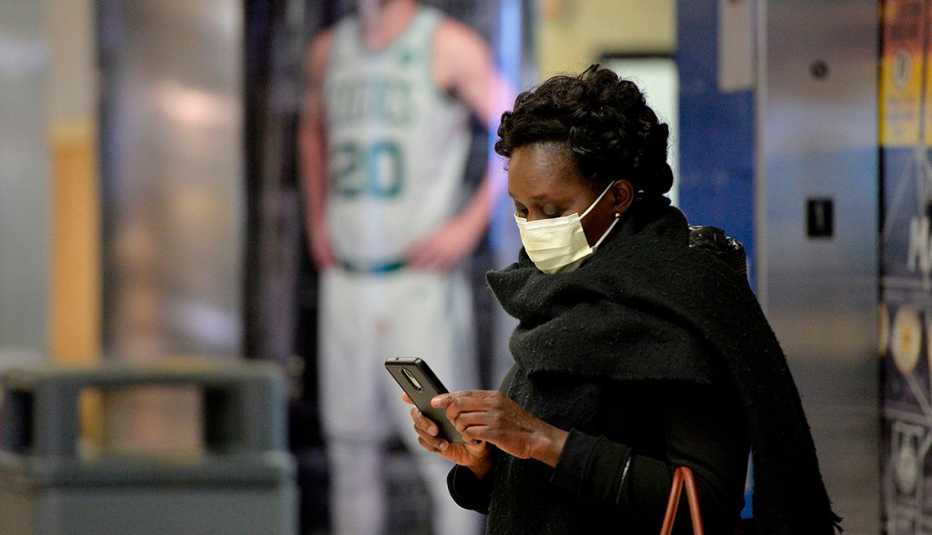 An African-American woman in a mask stands in TD Garden and checks her phone.