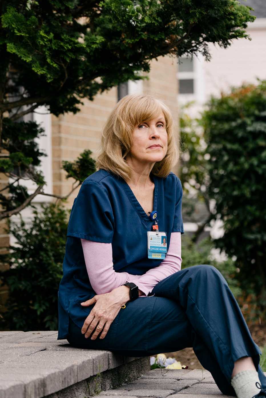 a middle aged nurse sits on the front steps of her building looking pensive