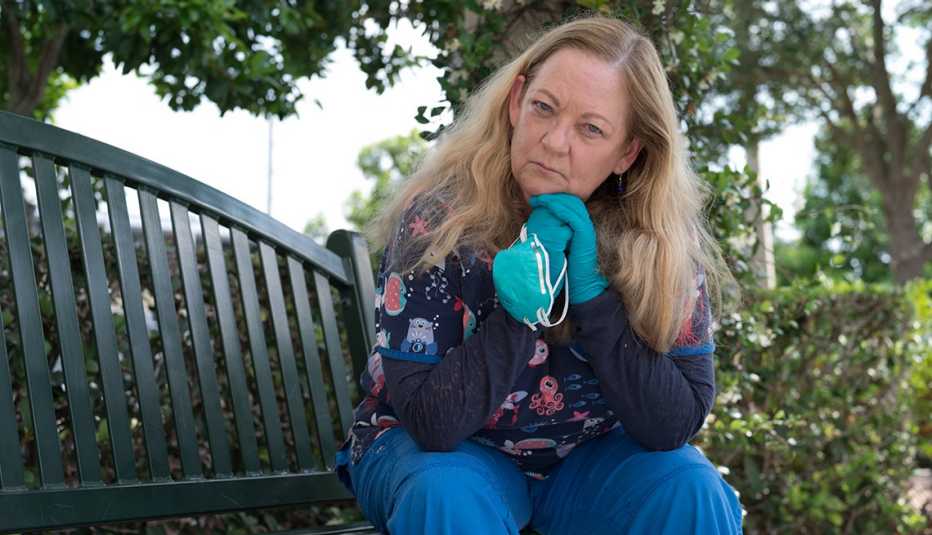 a nurse sits on a park bench outdoors resting her chin in her hands