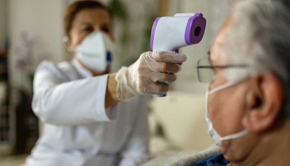 Doctor taking temperature of ill man. Both are wearing face masks.