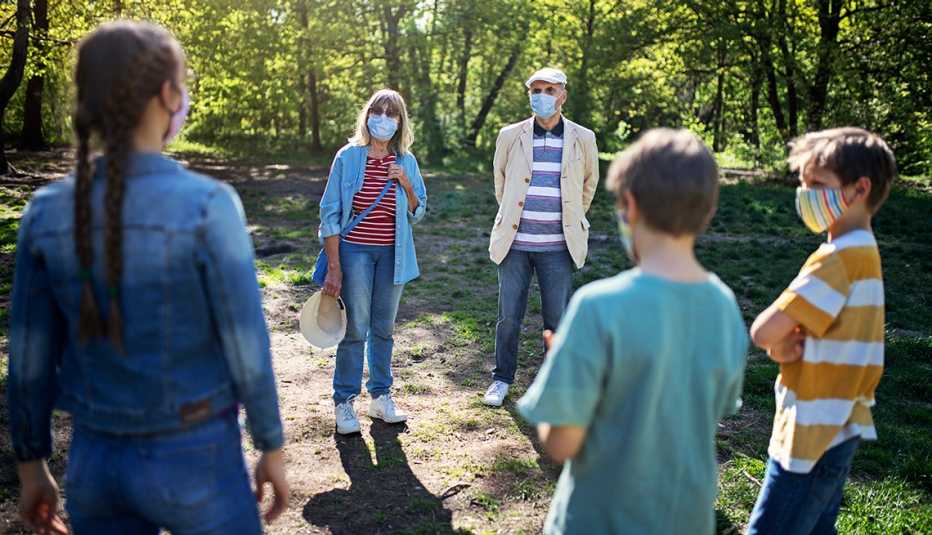 three siblings and their grandparents stand in a large circle in a park socially distanced and wearing masks