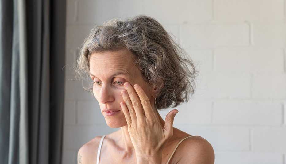 A woman with grey hair rubbing her eye to wipe away tear