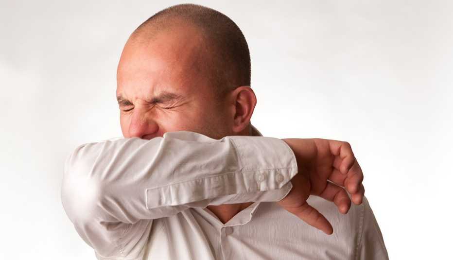 A man coughing/sneezing into his elbow/arm in order to stop the spread of disease.