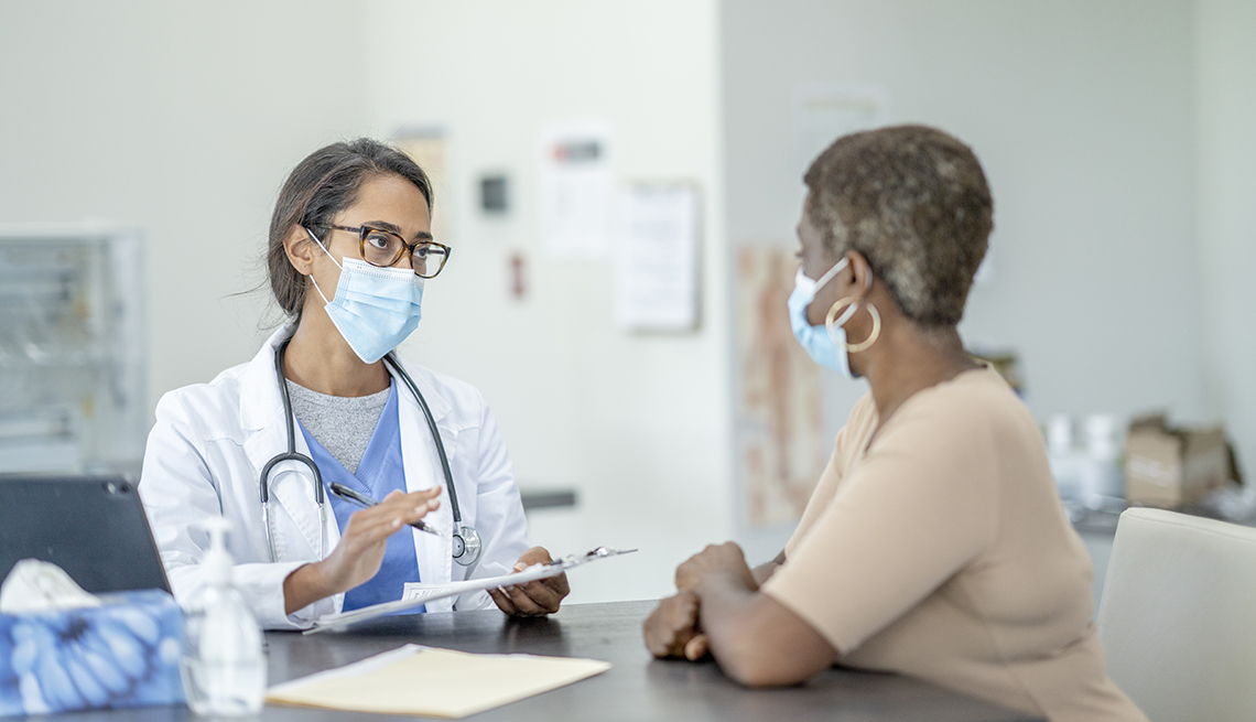 An African American patient talking with her doctor. Both are wearing face masks.