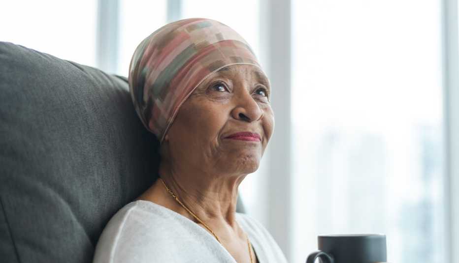 A black senior woman with cancer is wearing a scarf on her head and drinks tea.