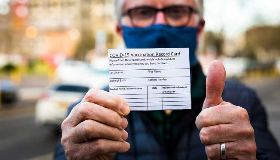 A man holding his vaccination record card and giving the thumb's up sign.