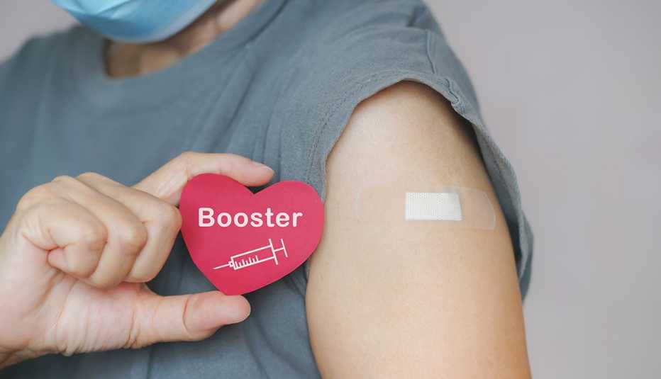 woman shows her booster shot bandaid and a paper heart that says booster