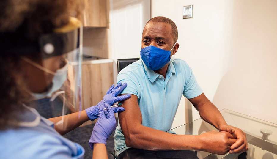 A nurse gives an African American man the coronavirus vaccine. Both are wearing face masks
