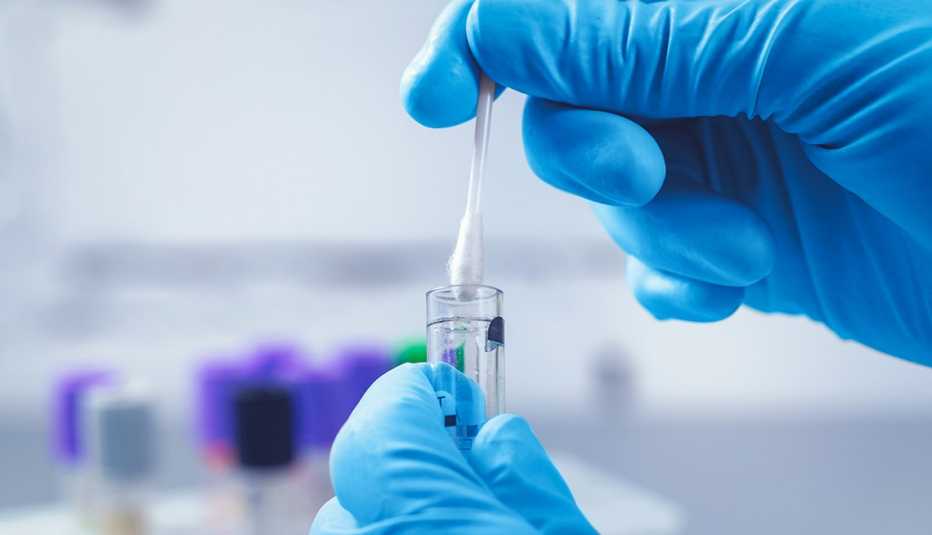 A person puts a swab into a test tube while wearing blue gloves