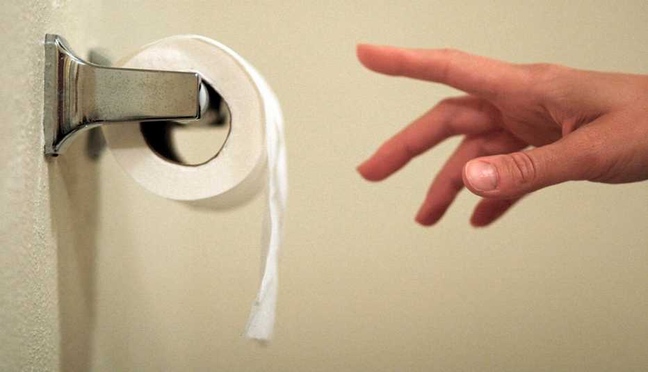 a hand reaching for a piece of toilet paper on a roll dispenser