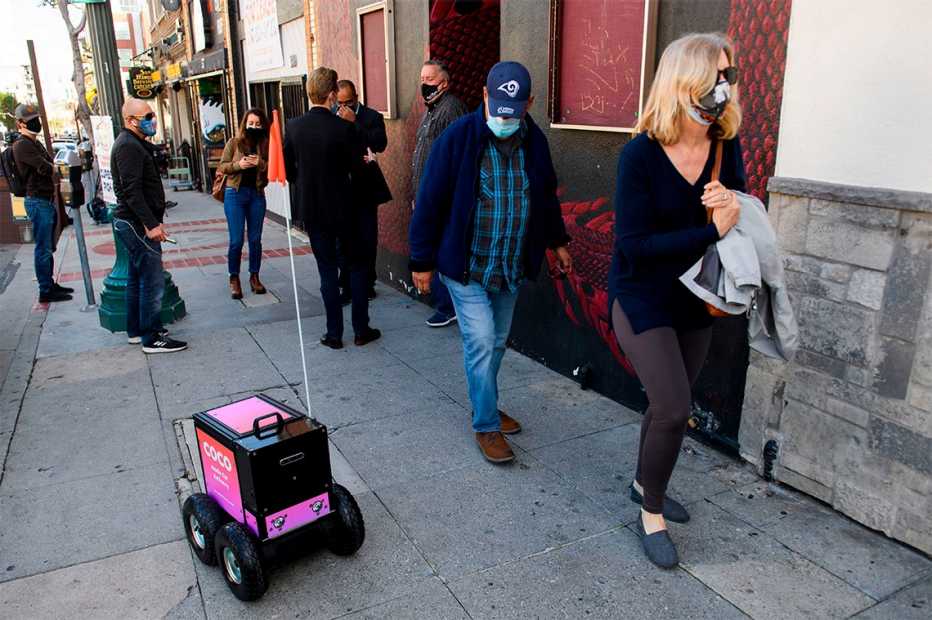 a remote controlled delivery robot on a sidewalk amongst pedestrians