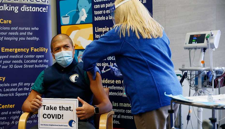 Man getting a covid-19 vaccine, holding a sign that says "Take that COVID!"
