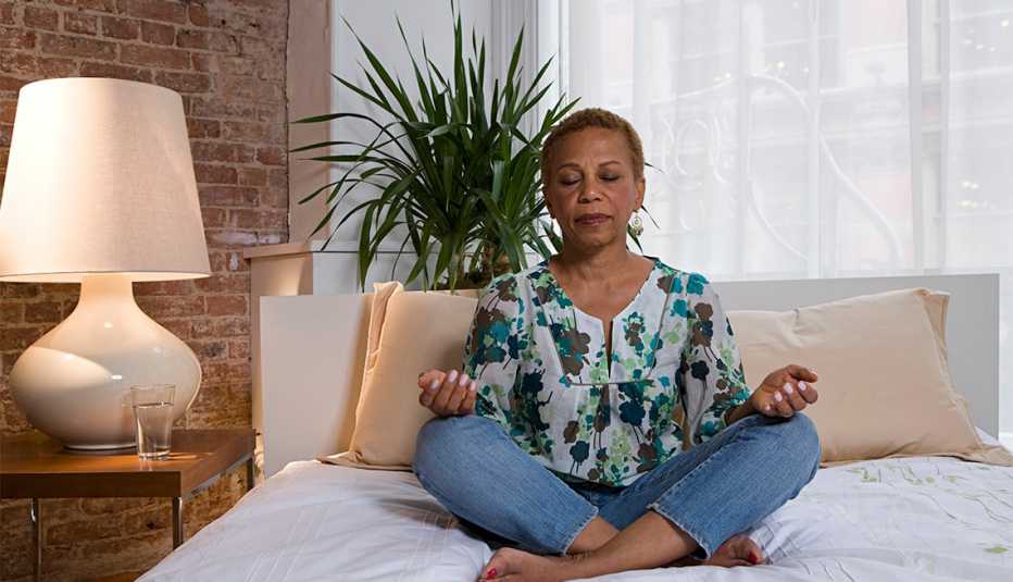 African American woman sits cross-legged on a bed and meditates