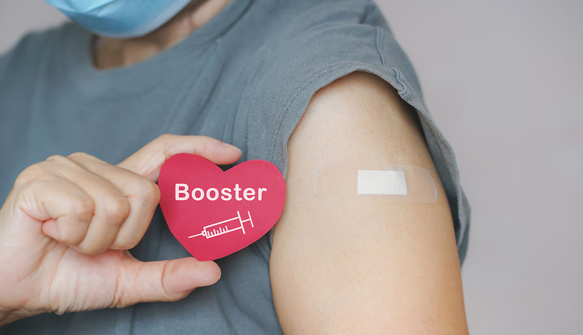 woman shows her booster shot bandaid and a paper heart that says booster