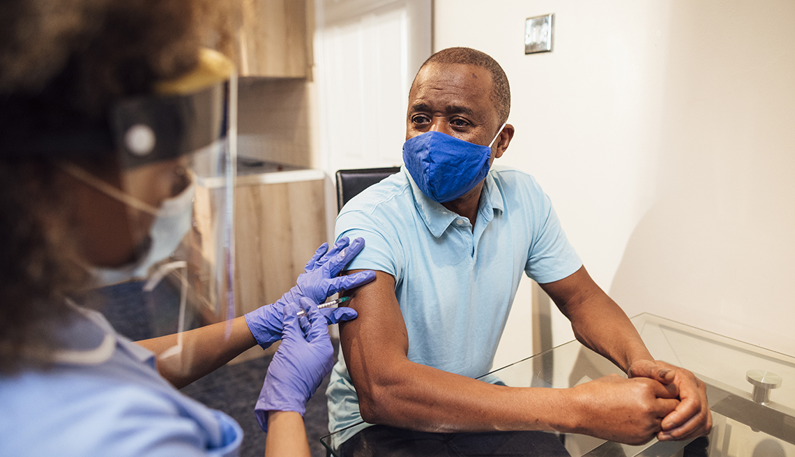 A nurse gives an African American man the coronavirus vaccine. Both are wearing face masks