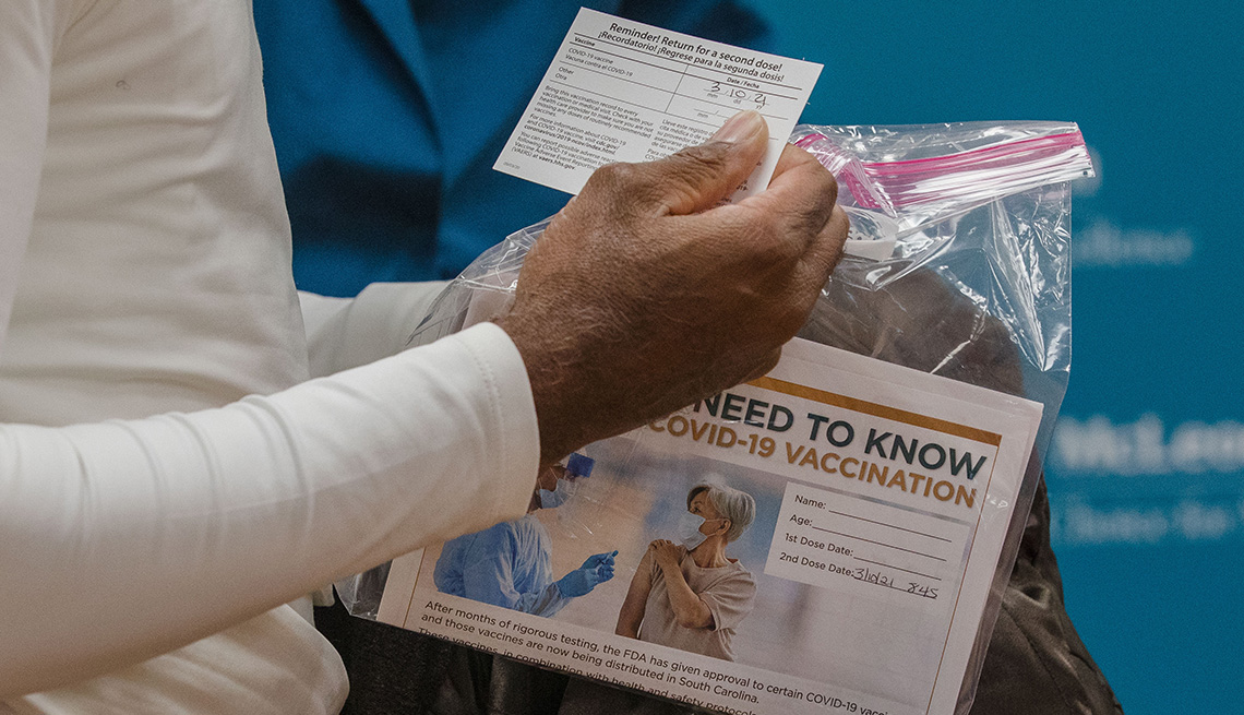 A patient holds a vaccination card and information packet after receiving the Pfizer-BioNTech vaccine