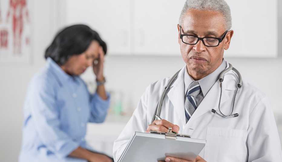 Male doctor writing on clipboard with patient suffering from a migraine in the backgroubnd.