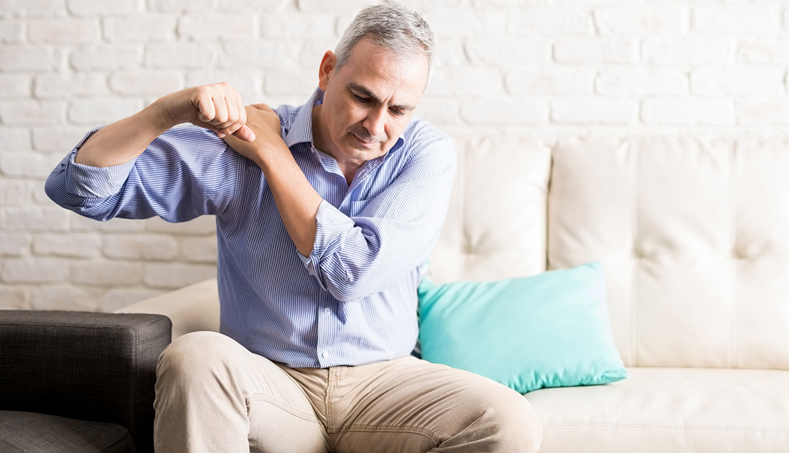 Middle aged man sitting on the sofa and holding painful shoulder with another hand.