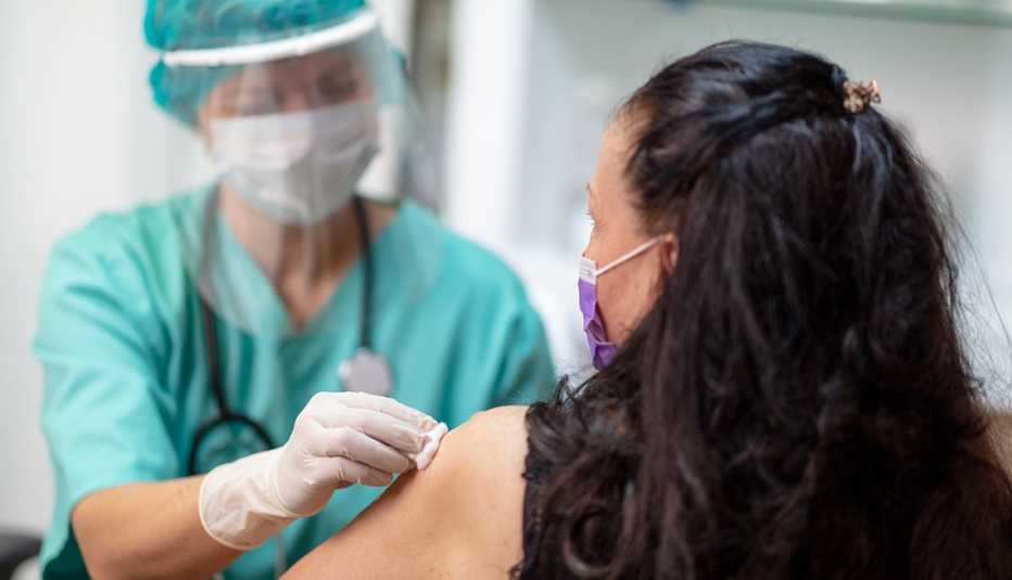 A doctor wearing a face shield prepares a woman's arm for vaccination