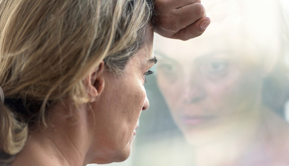 depressed woman looks at reflection in window