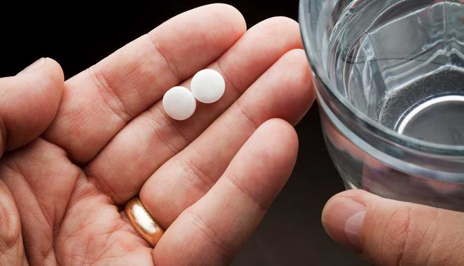 man's hands holding pain pills and a glass of water