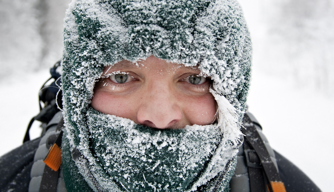 a close-up of a mans face, with frosty eyelashes, wearing a snow covered balaclava, winter background