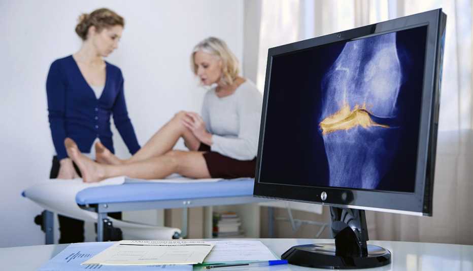 A bone scan display of a knee with arthritis in the foreground, while a woman in medical exam is explaining pain to health care provider in background.