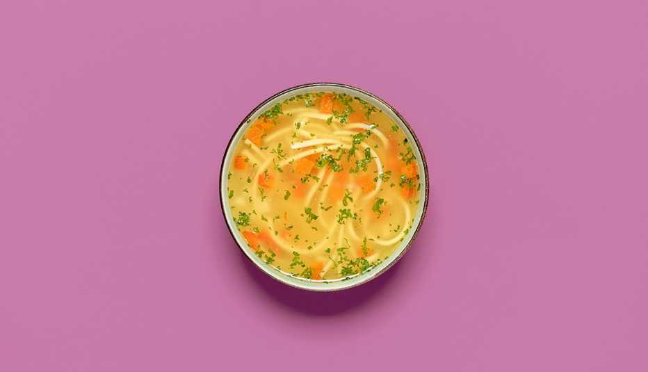 top view with a bowl of chicken soup with delicious noodles and carrots isolated on a light purple background