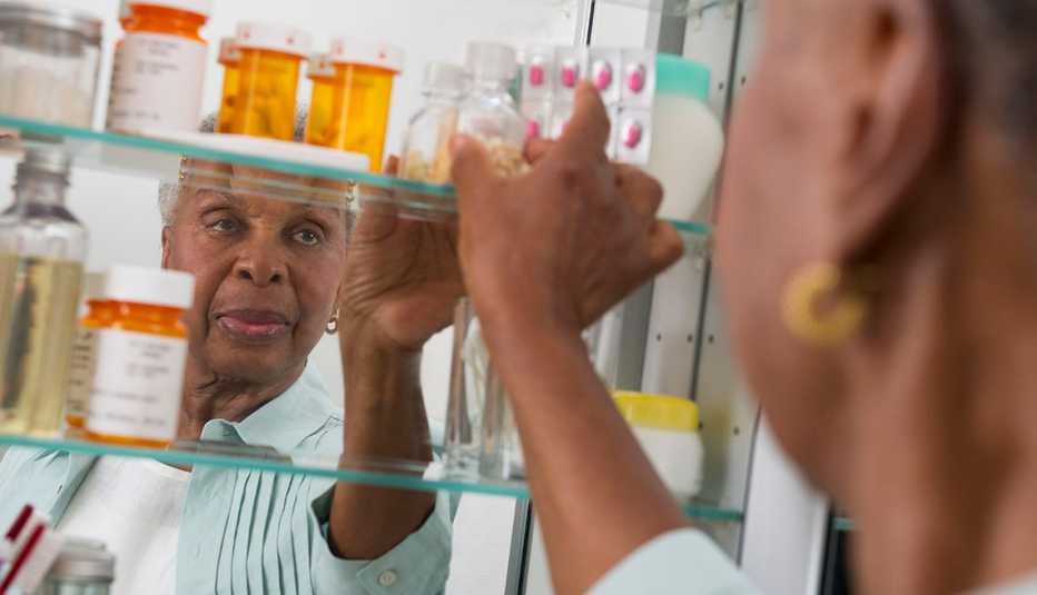 woman removing a bottle of pills from the medicine cabinet