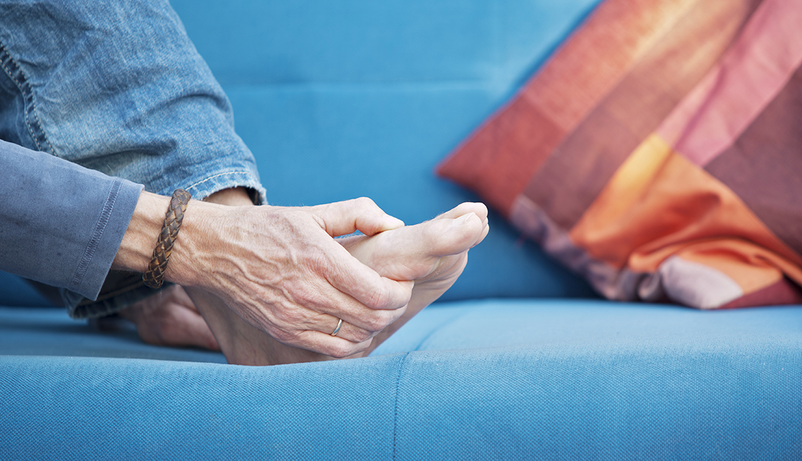 woman's hand massaging her foot, which is in pain while sitting on a blue couch